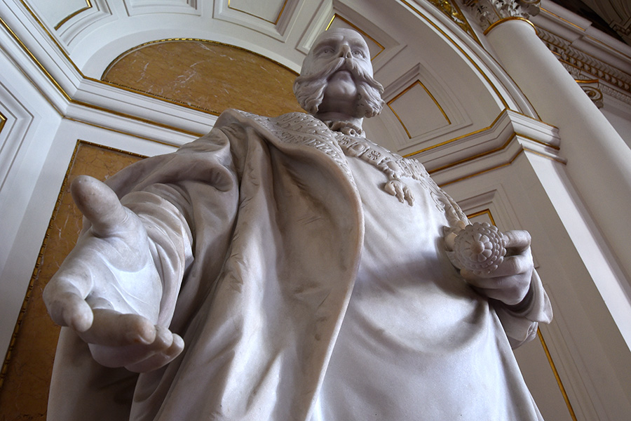 Ö1-Journalist Martin Haidinger und Historiker Peter Teibenbacher erzählen vor der Statue des bis heute präsenten Monarchen in der Aula der Uni Graz „die Österreich-Story“. Foto: Uni Graz/Schweiger 