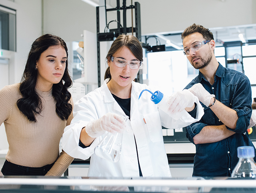Three students from the University of Graz prepare for their work in the BioHealth consortium in a laboratory. 