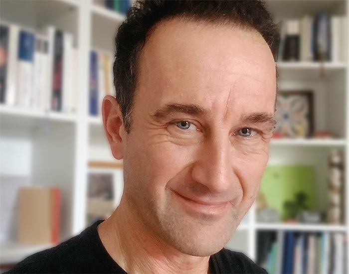 Christian Retscher lächelt in Kamera vor Bücherwand ©Christian Retscher