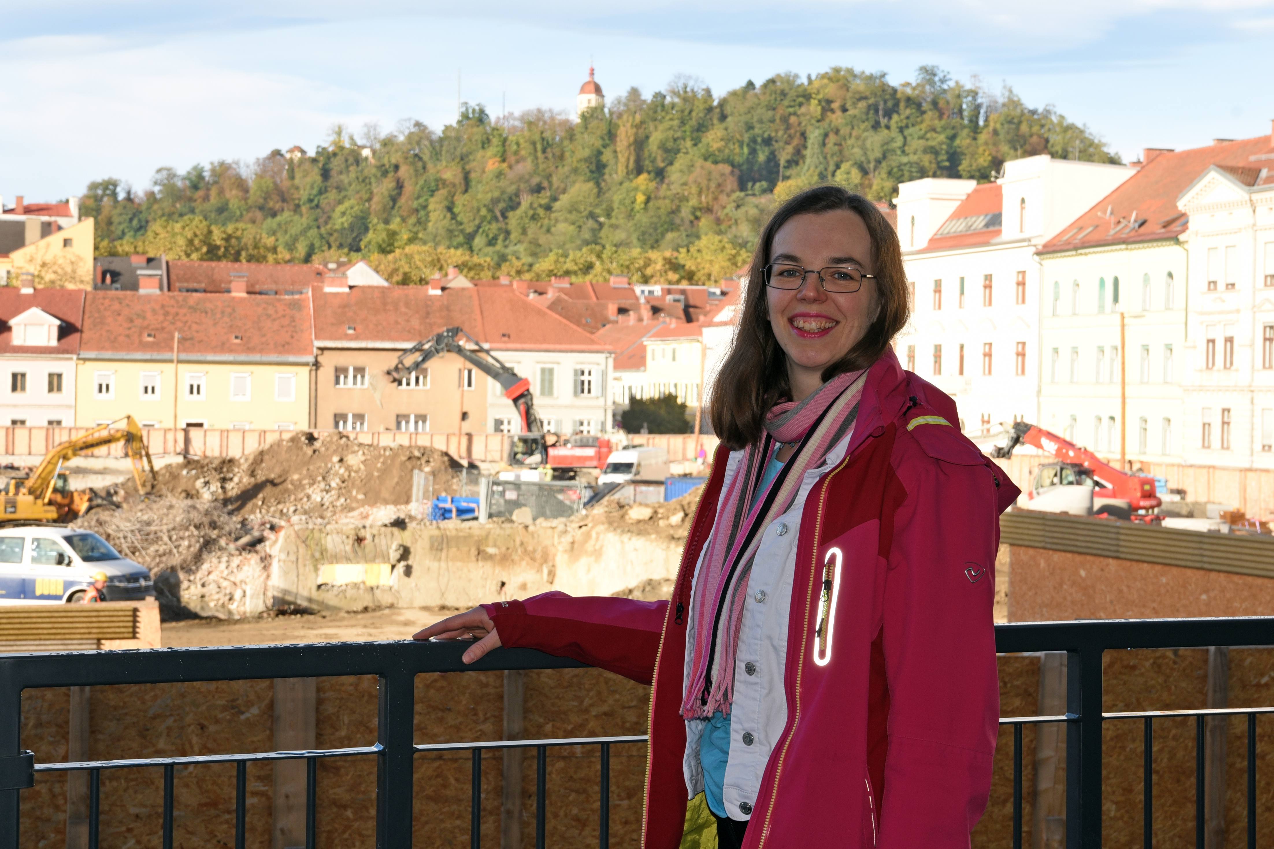 Caroline Delattre vor der Baustelle des neu entstehenden Graz Center of Physics, im Hintergrund der Schlossberg an einem sonnigen Tag ©Uni Graz/Eklaude