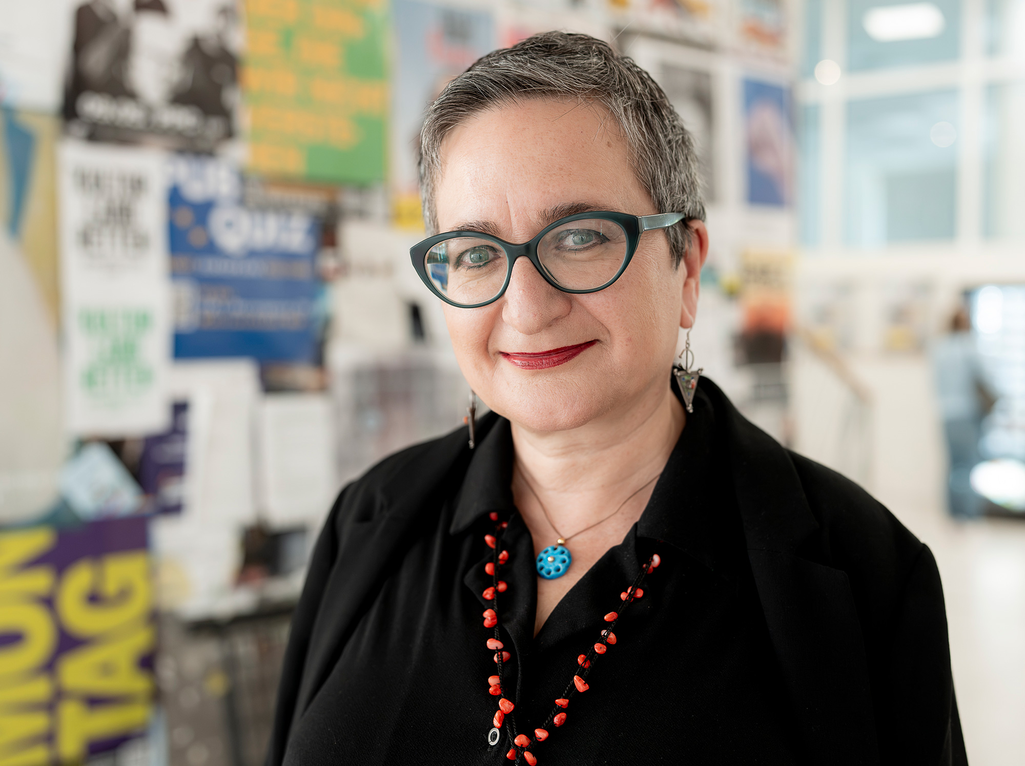 Şebnem Bahadır-Berzig, Portrait, im Hintergrund verschwommen bunte Plakate, aufgenommen im Wall-Zentrum der Uni Graz