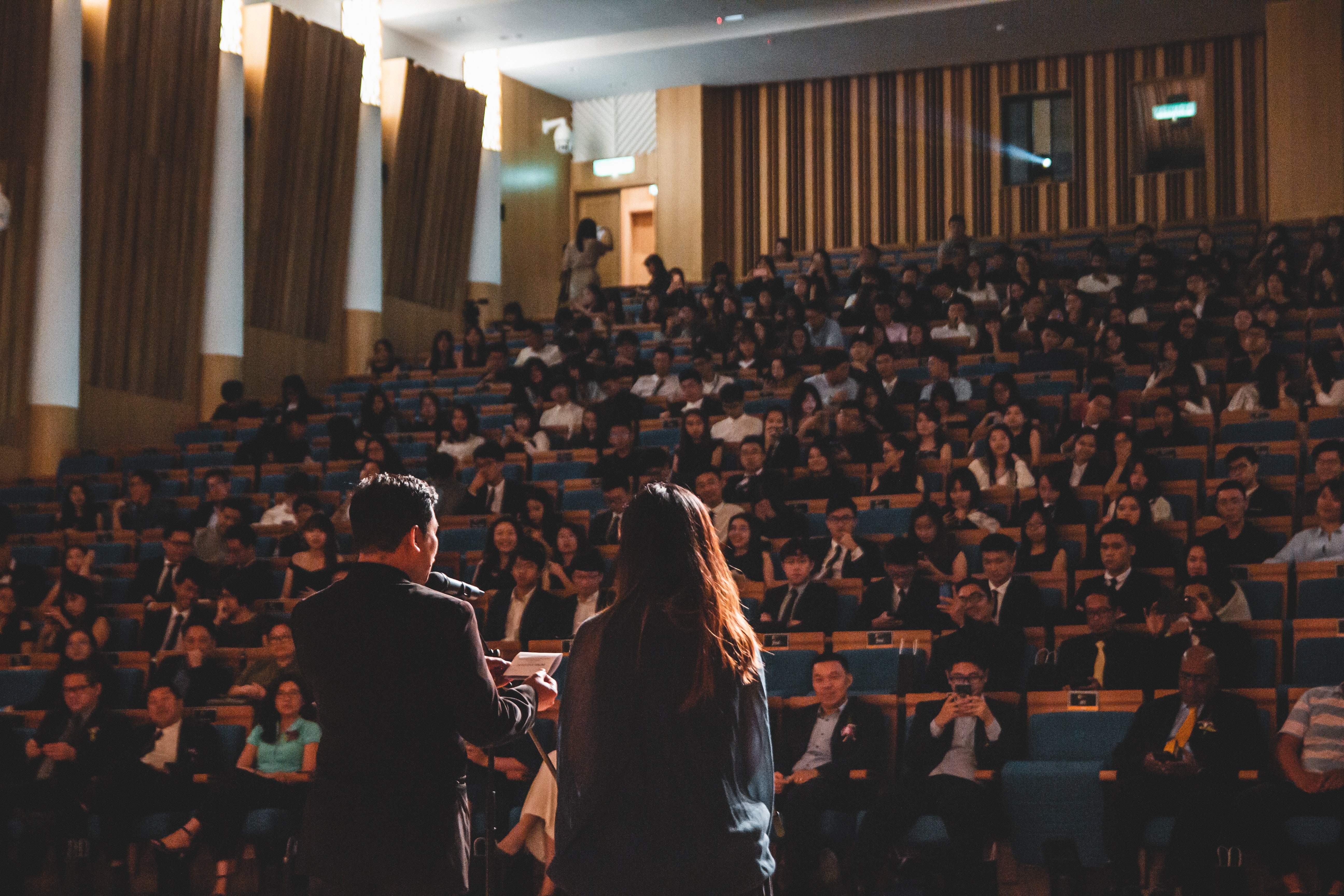 Zwei Personen von hinten vor einem großen Publikum; Hörsaalsituation ©Wan San Yip - unsplash.com