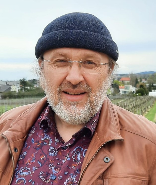Portrait of Stefan Baumgarten with leather jacket and woolly hat in front of a landscape 