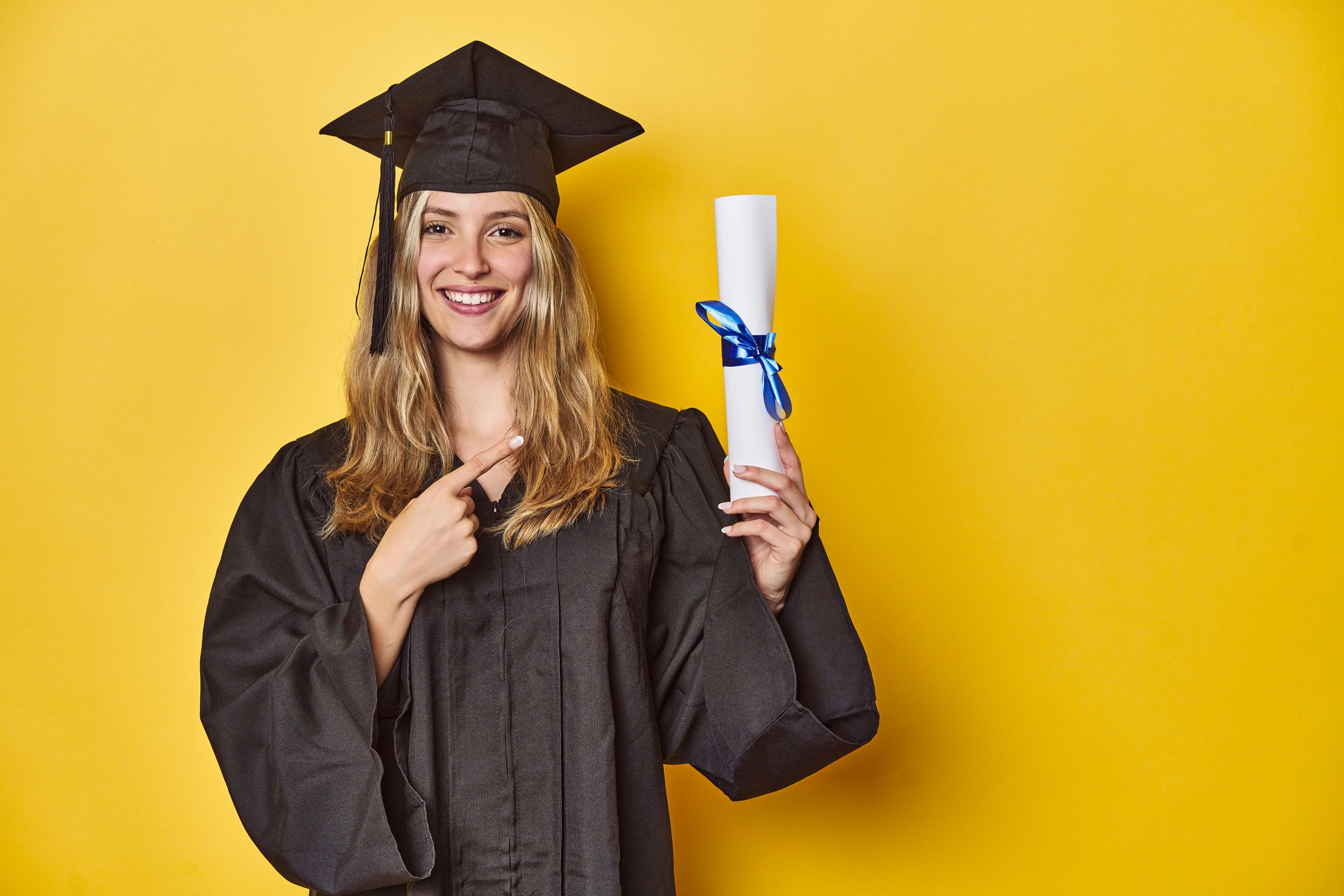 Junge Frau in Abschlussrobe mit Diplom vor gelbem Hintergrund. ©Asier - stock.adobe.com