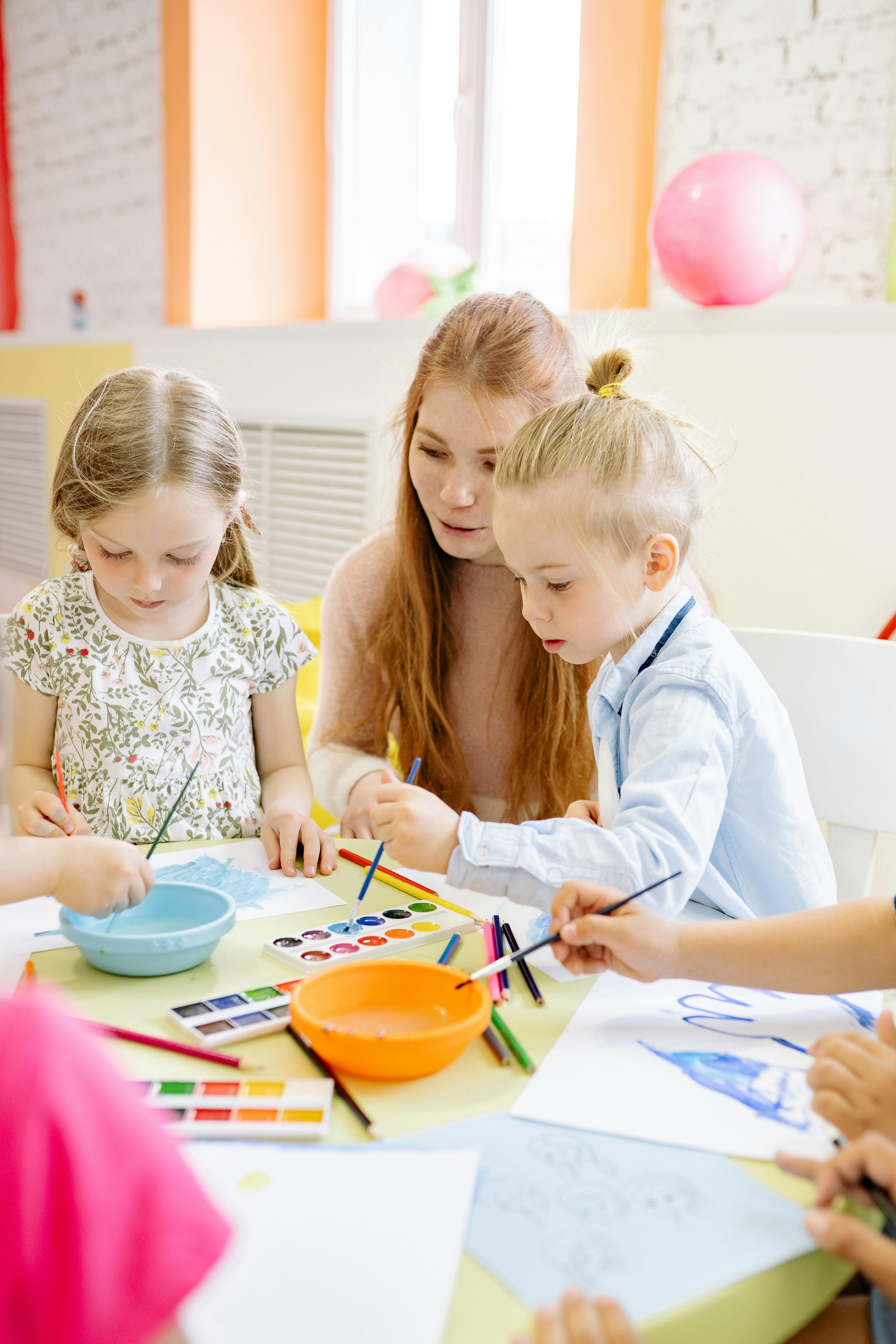 Junge Frau sitzt mit zwei Kindern an einem Tisch und symbolisiert die Schwerpunkte innerhalb des Projekts Elementarpädagogik fördern ©yankrukov/pexels