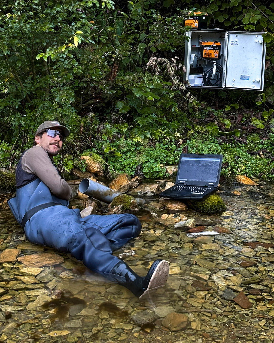 Ein Mann liegt mit Regenhose im Wasser und macht Messungen. 