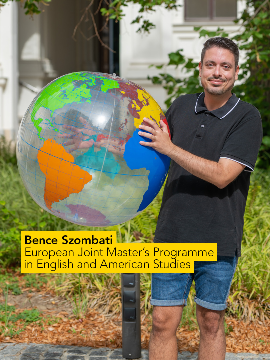 Ein Mann mit dunklem Oberteil und Jeans hält einen Globus und zeigt auf Frankreich. 
