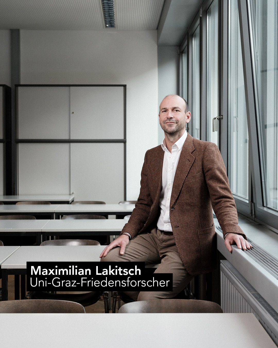 Mann in brauner Hose und Sakko sitzt auf Tisch. Davor die Aufschrift "Maximilian Lakitsch Uni-Graz-Friedensforscher" 