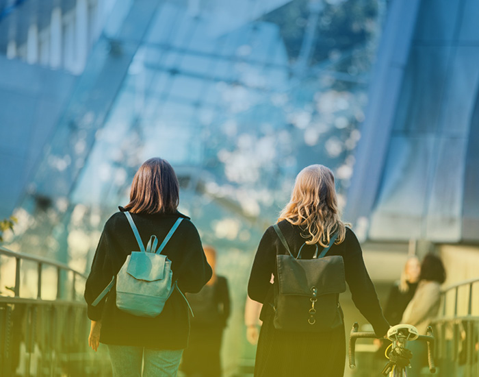 You see two young women from behind, walking towards the university, one of them pushing a bicycle ©Uni Graz/Kanizaj