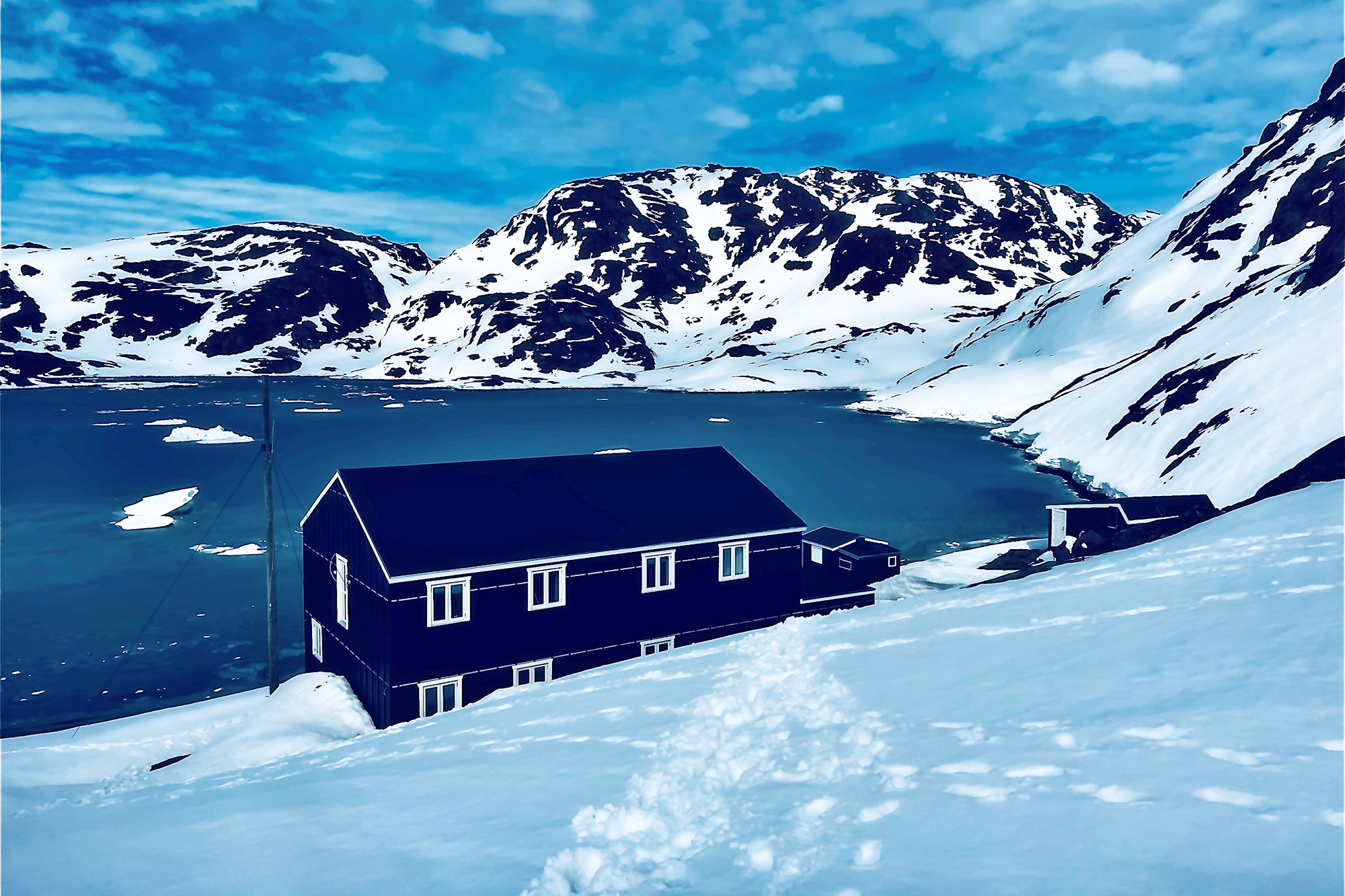 Ein Haus nahe eines Fjords mit schneebedeckten Bergen