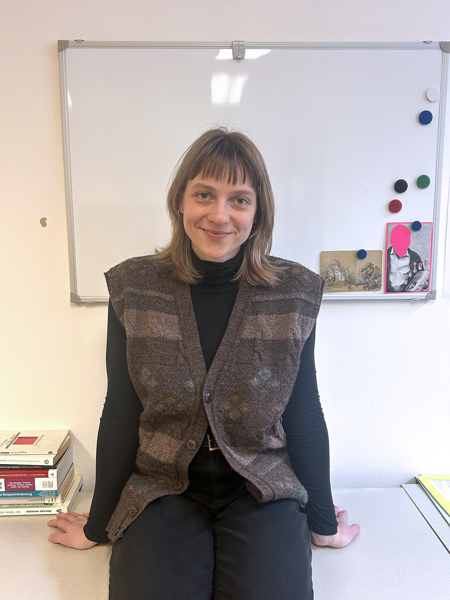 Portrait einer jungen Frau mit schulterlangen hellbraunen Haaren vor einer weißen Tafel