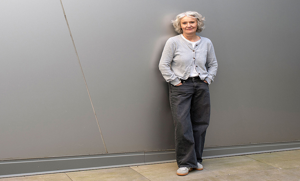 Claudia Traunmüller, stehend, an eine graue Wand gelehnt