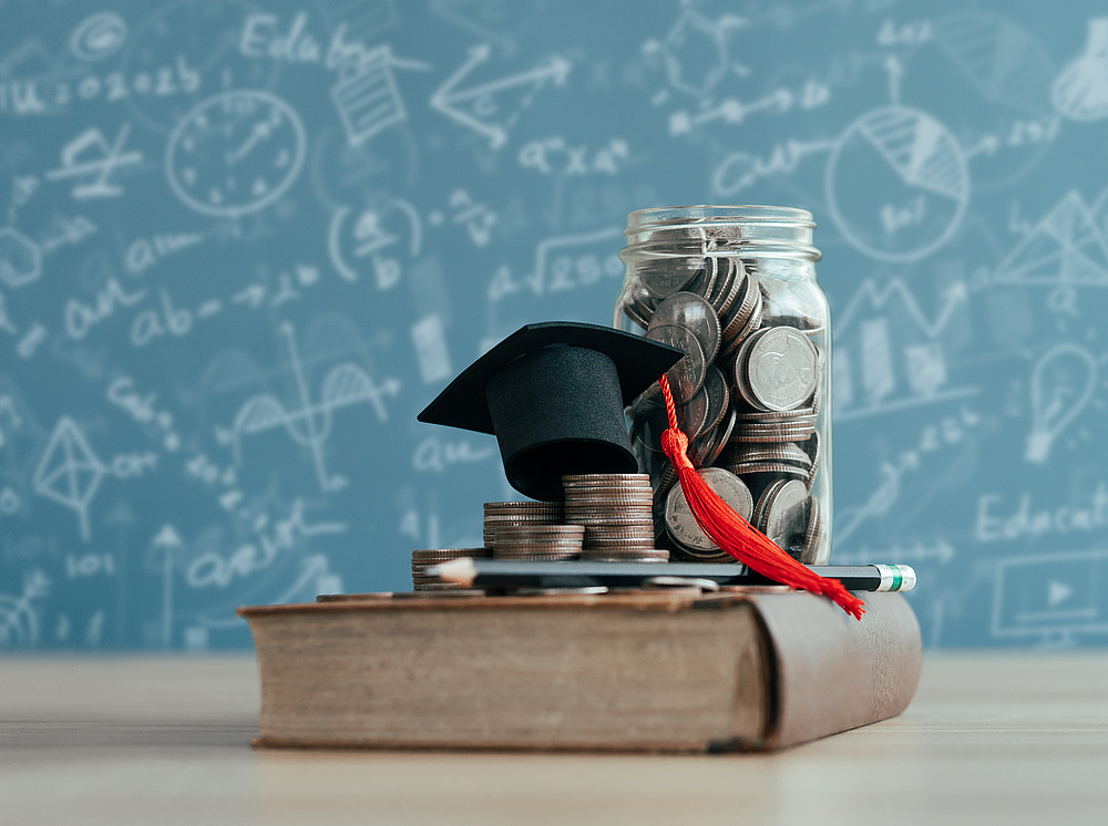 doctoral hat and a drink glass of coins on a book ©By narawit; stock.adobe.com