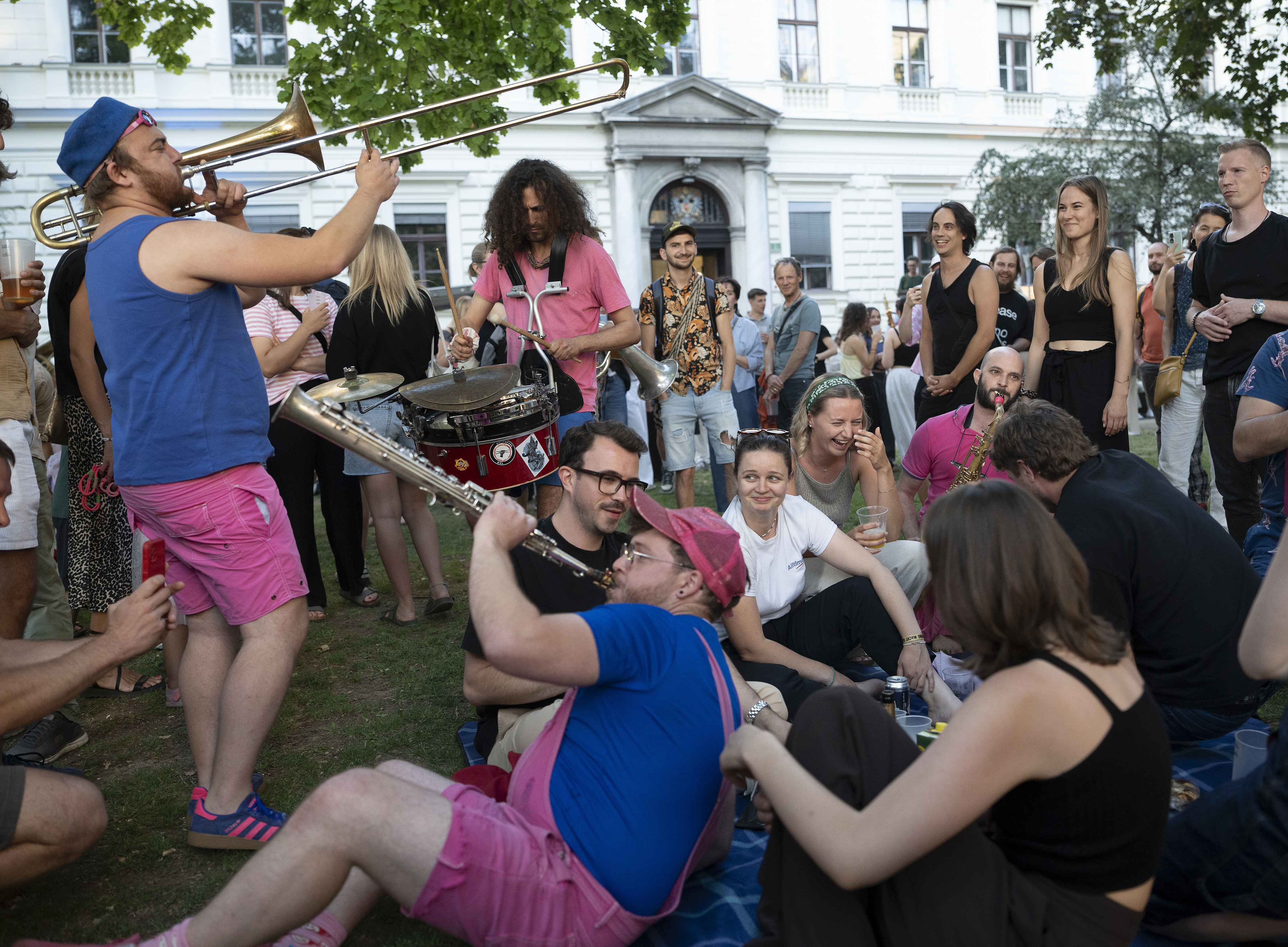 A crowd on the lawn in front of the university building; several people are playing music on a trombone, saxophone and drum, whilst others sit in a circle and listen. ©Uni Graz/Fuchs