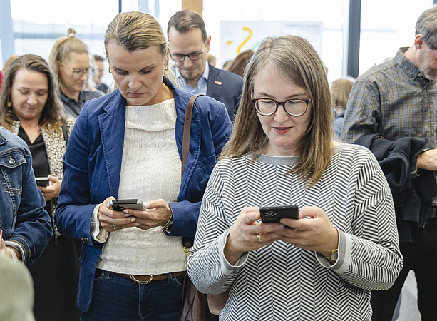 Gäste bedienen ihre Smartphones bei einer Veranstaltung; im Vordergrund tippt eine Frau mit Brille auf ihrem Handy. ©@foto-gasser.at