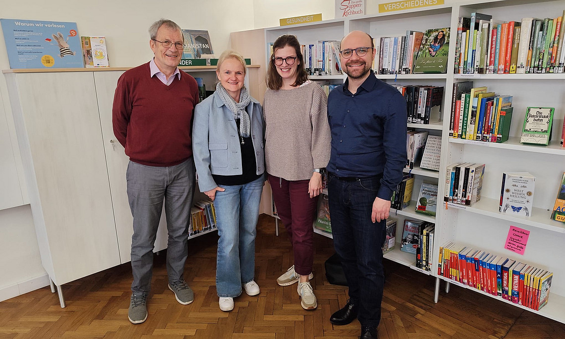 zwei Frauen und zwei Männer stehen vor einem Bücherregal und lächeln