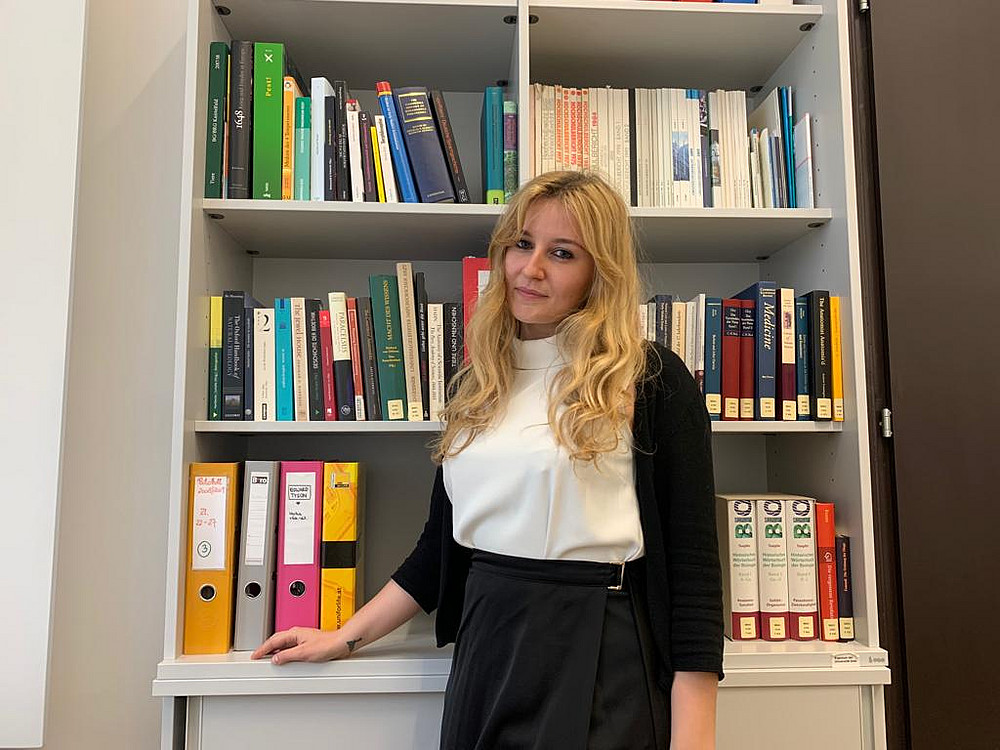 Lisa Brunner is standing in front of a bookshelf, her hand resting on the shelf and looking towards the camera. ©privat