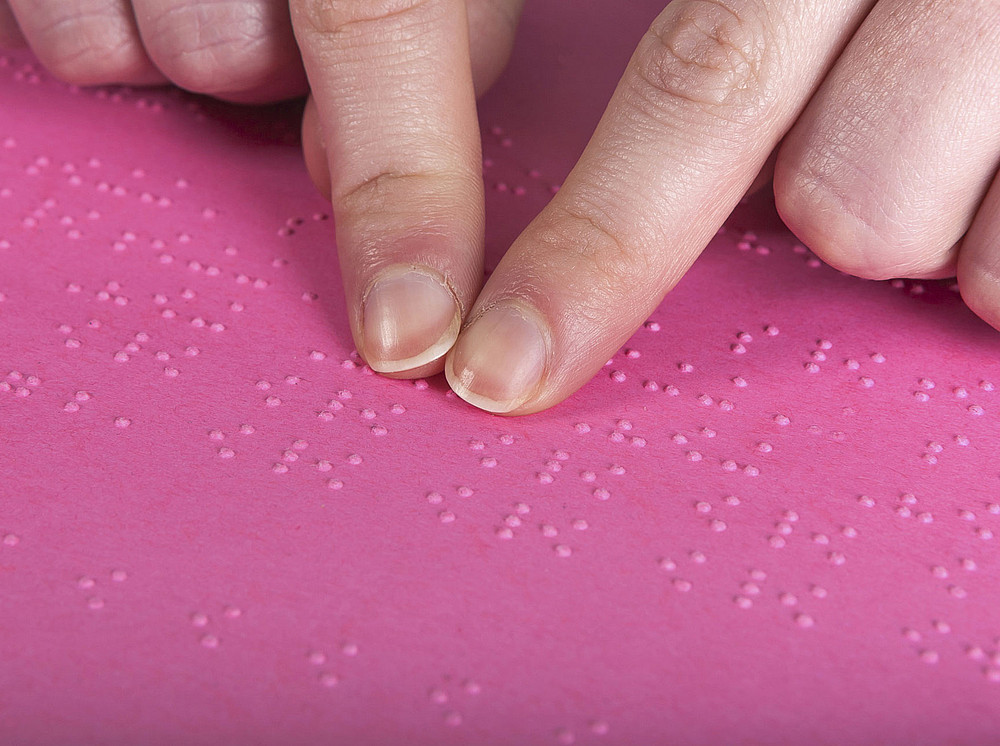 Zwei Zeigefingern erfühlen die Brailleschrift auf pinkem Papier. ©SIMEON CHATZILIDIS
