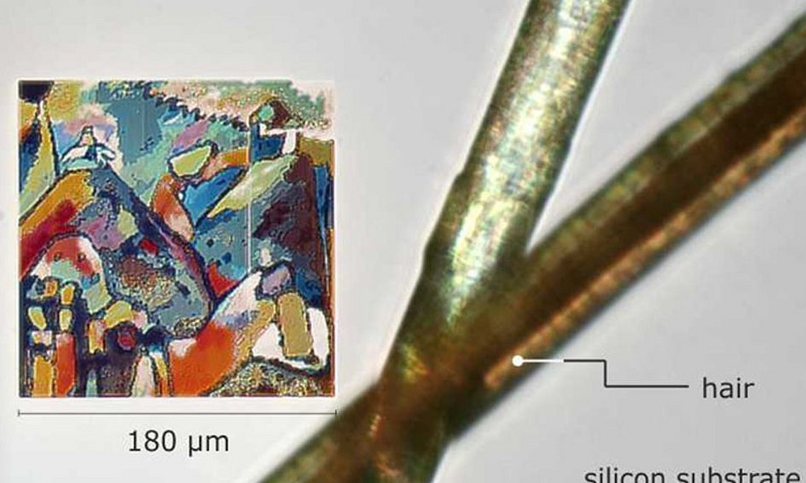 Reproduktion eines Gemäldes von Kandinsky auf Mikrometerskala durch optische Resonanzen von Löchern in Silizium, abgebildet neben einem menschlichen Haar (Bild: M. Hentschel)