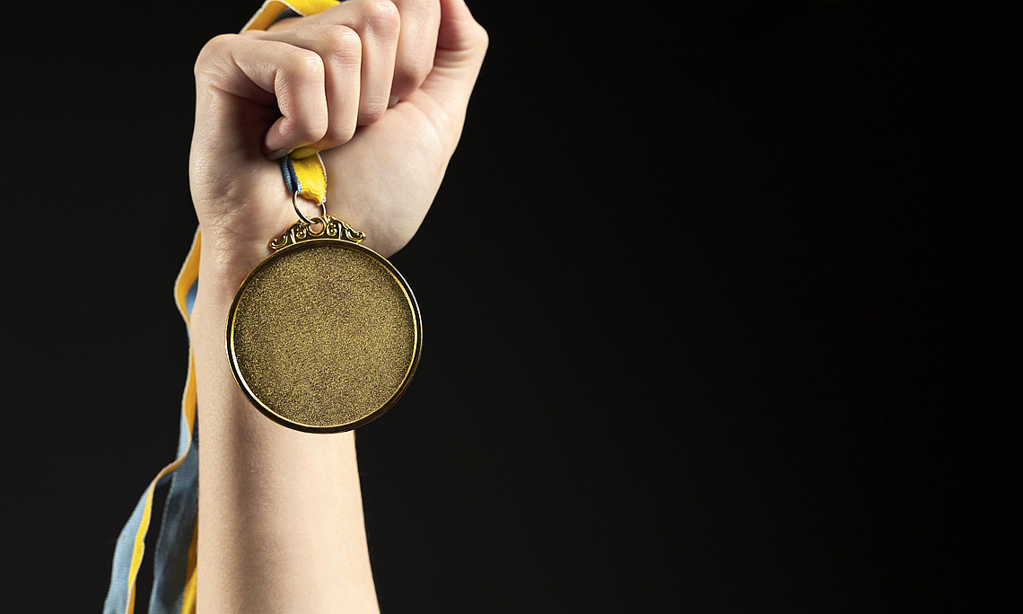 Hand die eine Medaille in die Höhe hält