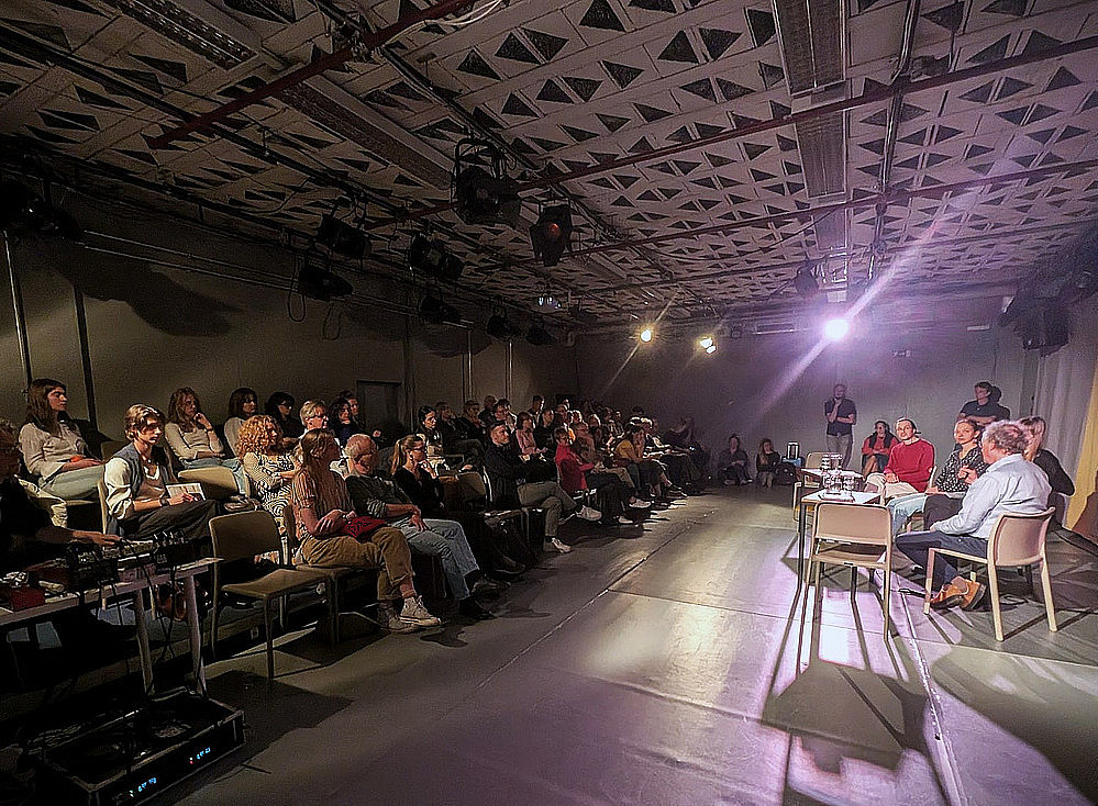Publikum bei Diskussion mit Bühnenhintergrund. ©(c) Josef Mühlbauer