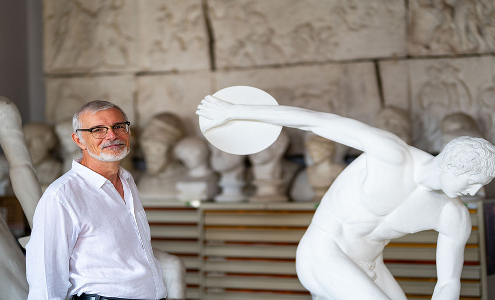 Altertumsexperte Werner Petermandl im Gipsmuseum neben der bekannten Statue des Diskuswerfers im Gipsmuseum der Uni Graz. Ersteht links im Bild und trägt ein weißes Hemd. Das Foto hat eine leichte Hintergrundunschärfe.