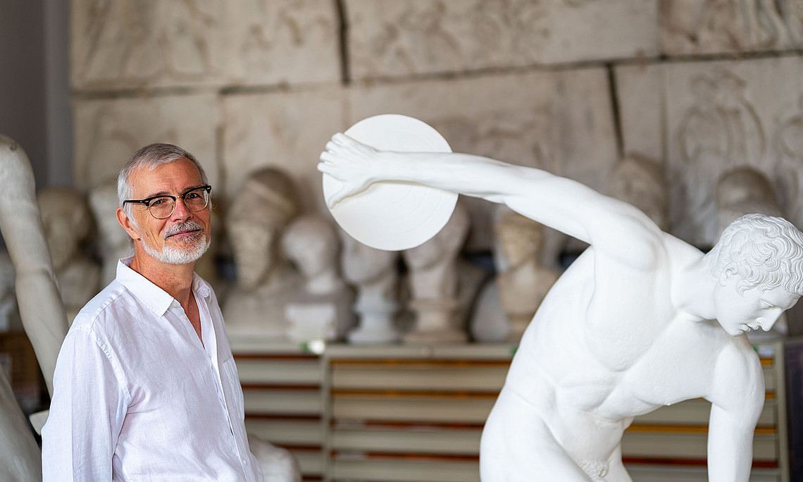 Altertumsexperte Werner Petermandl im Gipsmuseum neben der bekannten Statue des Diskuswerfers im Gipsmuseum der Uni Graz. Ersteht links im Bild und trägt ein weißes Hemd. Das Foto hat eine leichte Hintergrundunschärfe.