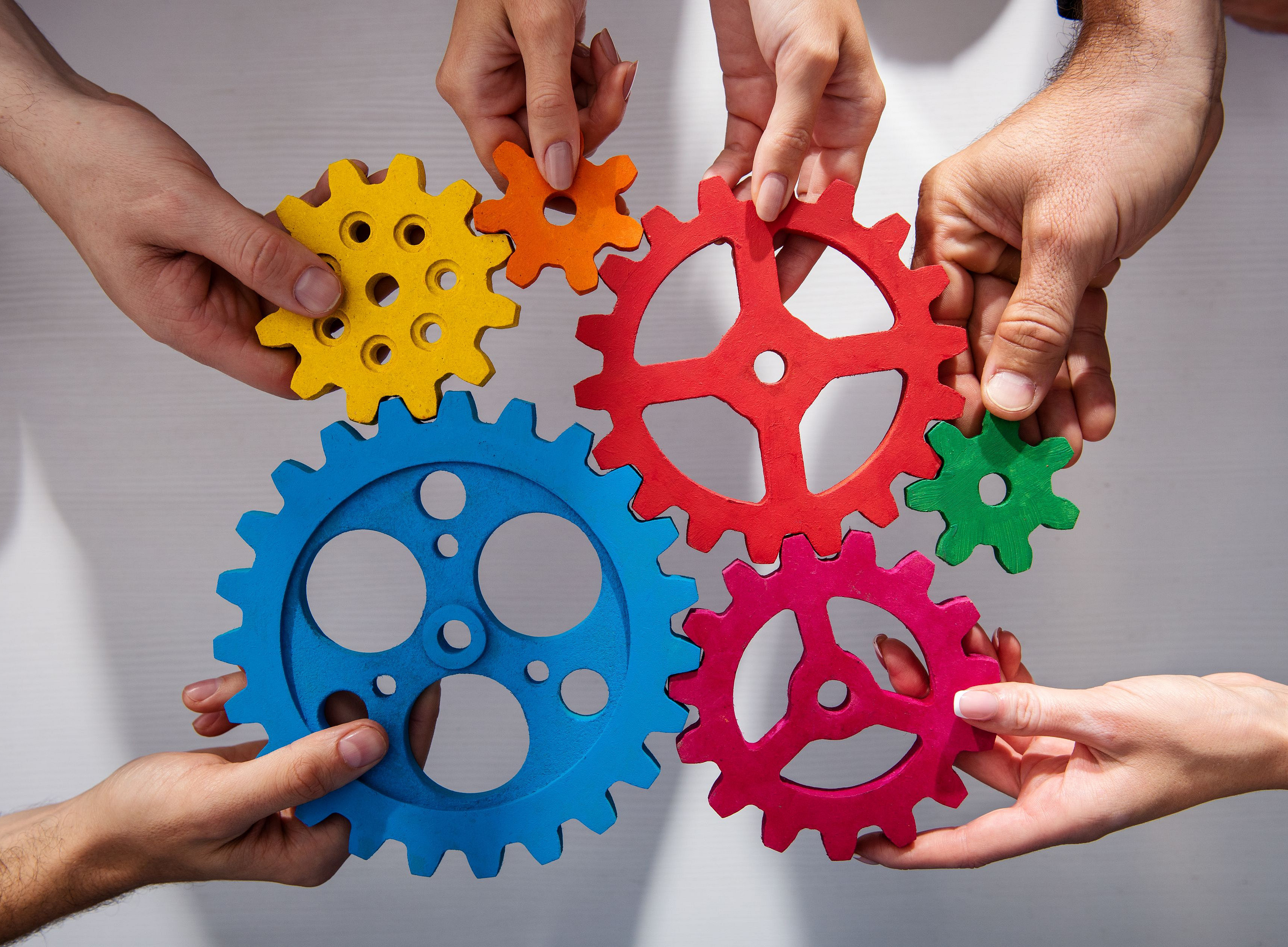 Bunte Zahnräder die von Händen gehalten werden. ©Alphaspirit - stock.adobe.com