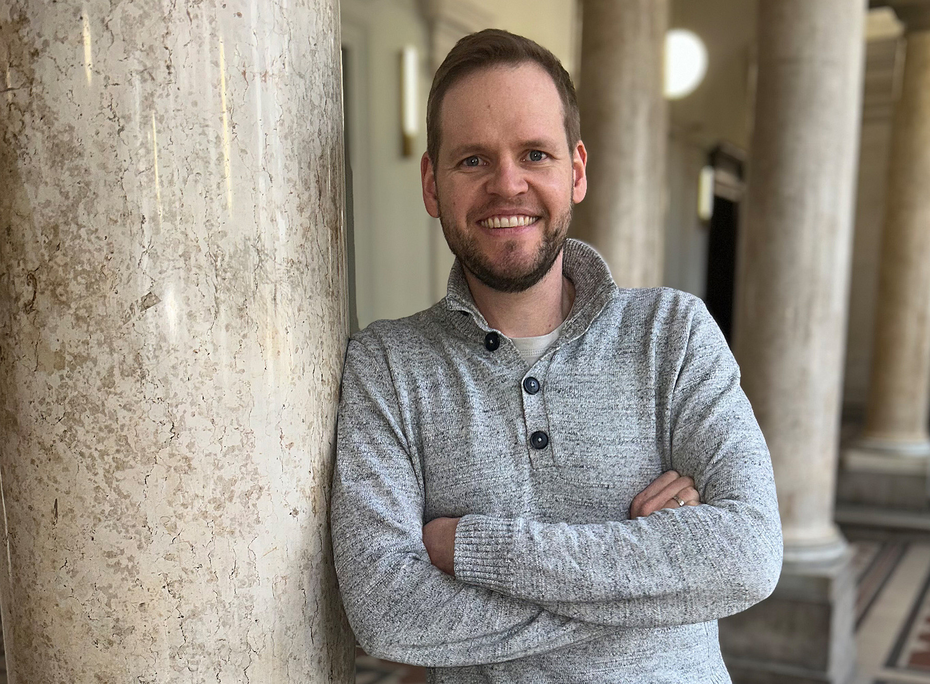 Dominik Sorger lehnt mit verschränkten Armen an einer Säule im Foyer des Uni-Graz-Hauptgebäudes 