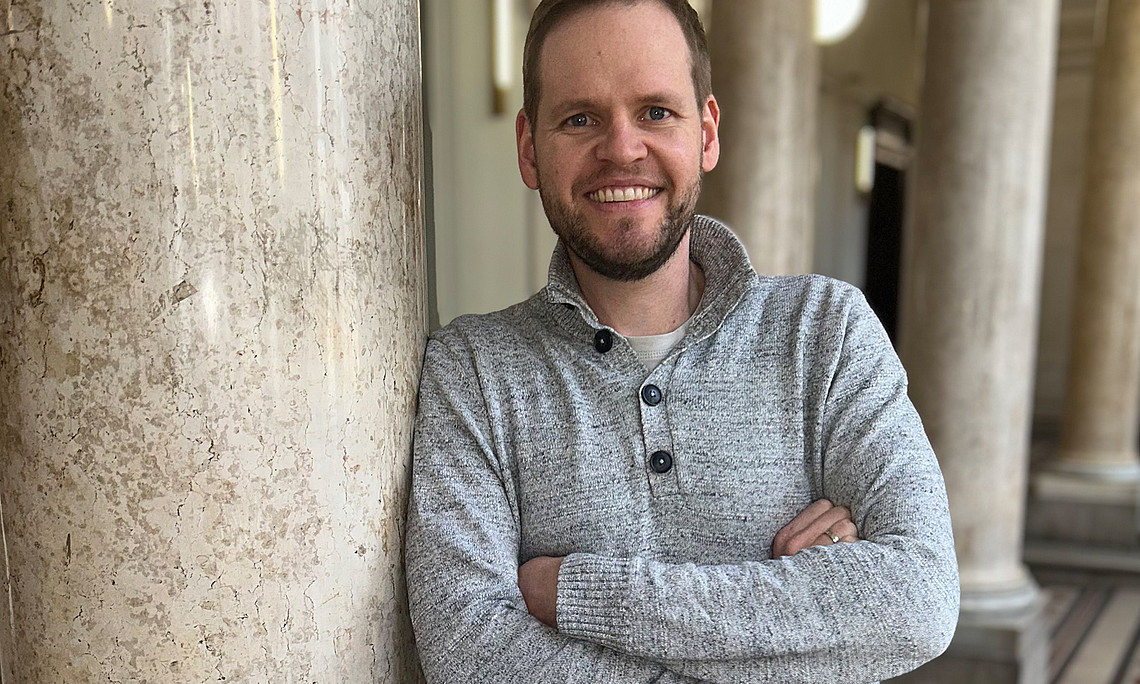 Dominik Sorger lehnt mit verschränkten Armen an einer Säule im Foyer des Uni-Graz-Hauptgebäudes