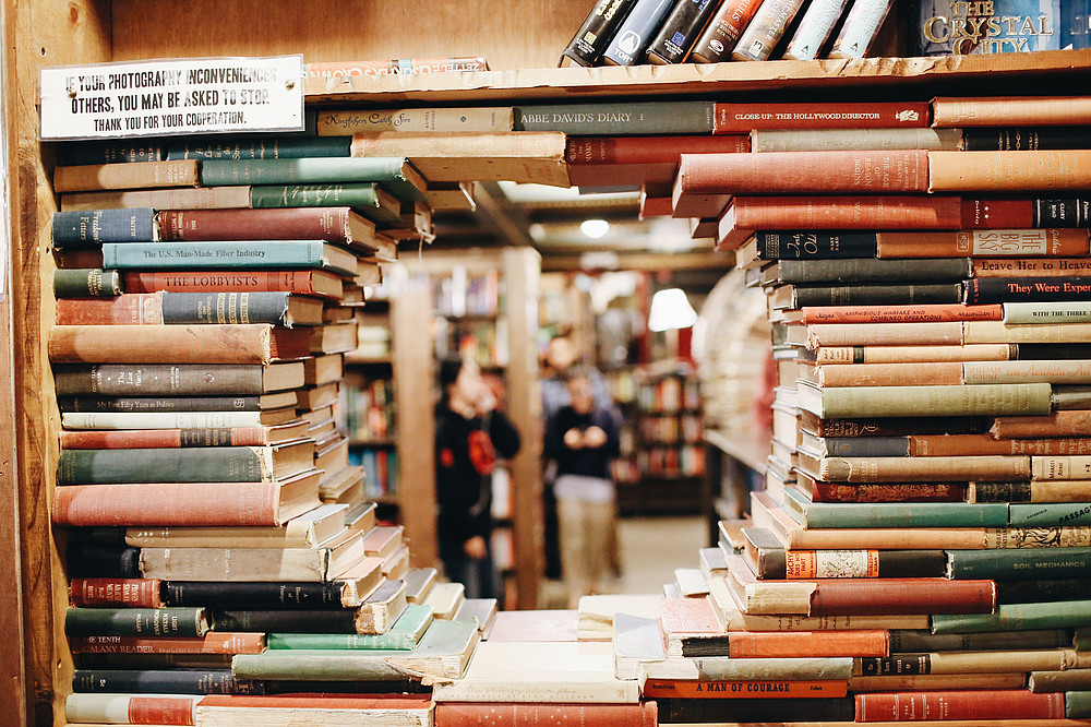 Gestapelte Bücher ergeben ein Loch, das die Sicht auf eine Bibliothek freigibt. ©Fallon Michael - unsplash.com