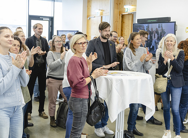 Eine Gruppe von Gästen applaudiert an Stehtischen in einem Veranstaltungsraum. ©@foto-gasser.at