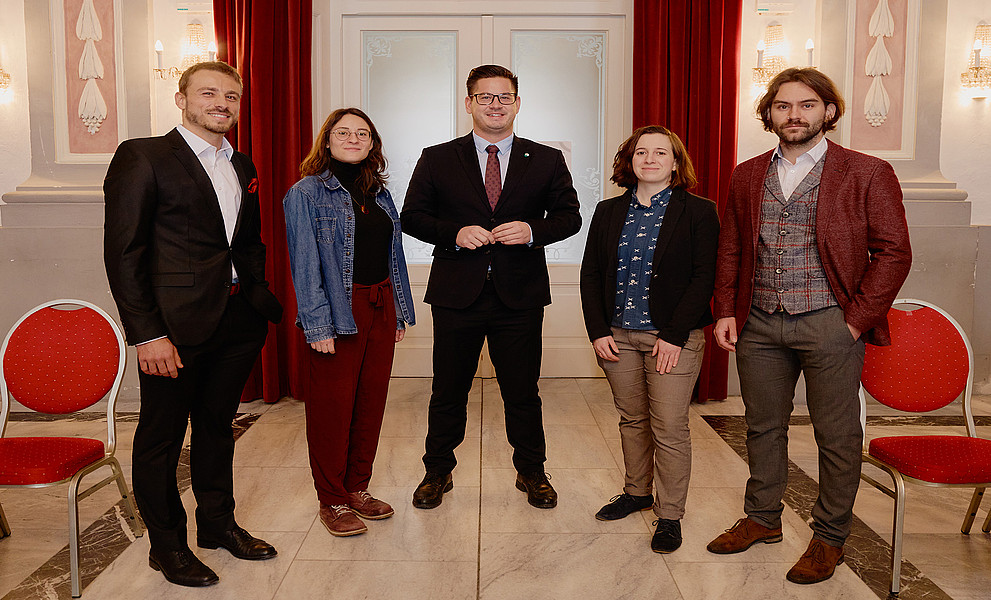Gruppenfoto von den Träger:innen der Sportwissenschaftlichen Preise 2025 mit dem Landtagsabgeordneten Gerhard Hirschmann in der Mitte im Festsaal des Meerscheinschlössls