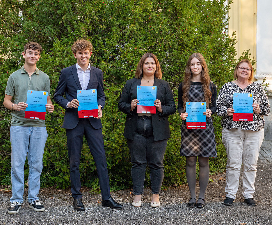 Five young adults are standing in front of a bush next to a building; some are dressed formally, and they are holding blue certificates in their hands. ©Uni Graz/Weber