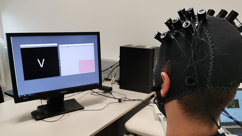 Eine Person die eine NIRS Haube trägt sitzt vor einem Monitor und übt Neurofeedback ©Silvia Kober