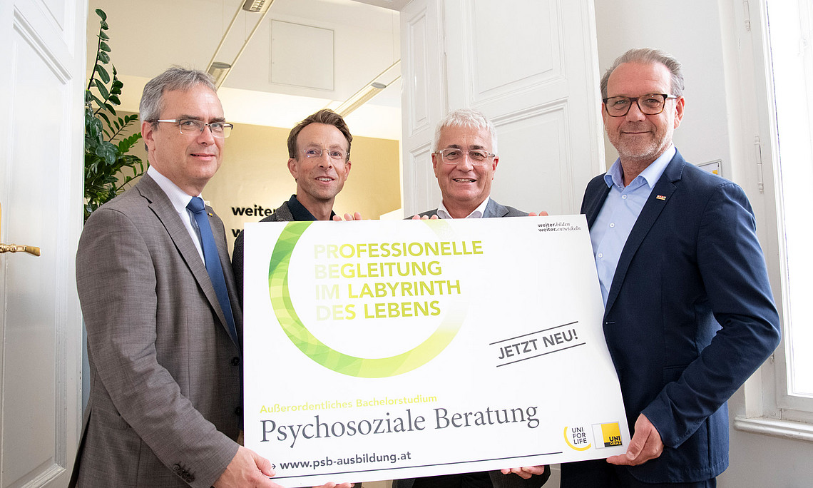 Vier Personen stehen mit einem Schild vor einer weißen Tür