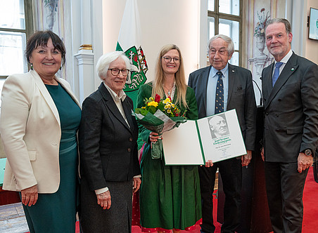 Eine Gruppe von fünf Menschen, eine Frau in der Mitte hält eine Urkunde. ©LandSteiermark/Binder