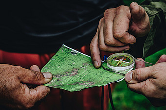 Zwei Paar Hände, die auf eine Landkarte mit einem Kompass zeigen.
