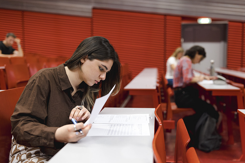 Eine Studentin sitzt mit einem Fragebogen im Hörsaal