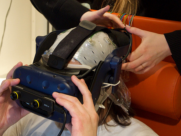 Eine Versuchsperson mit aufgesetzter VR Brille und EEG Kappe ©Silvia Kober