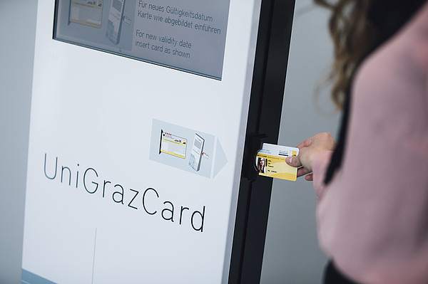 Nahaufnahme eines Automaten, in den eine Person ihre UniGrazCard einfügt um sie automatisch zu verlängern