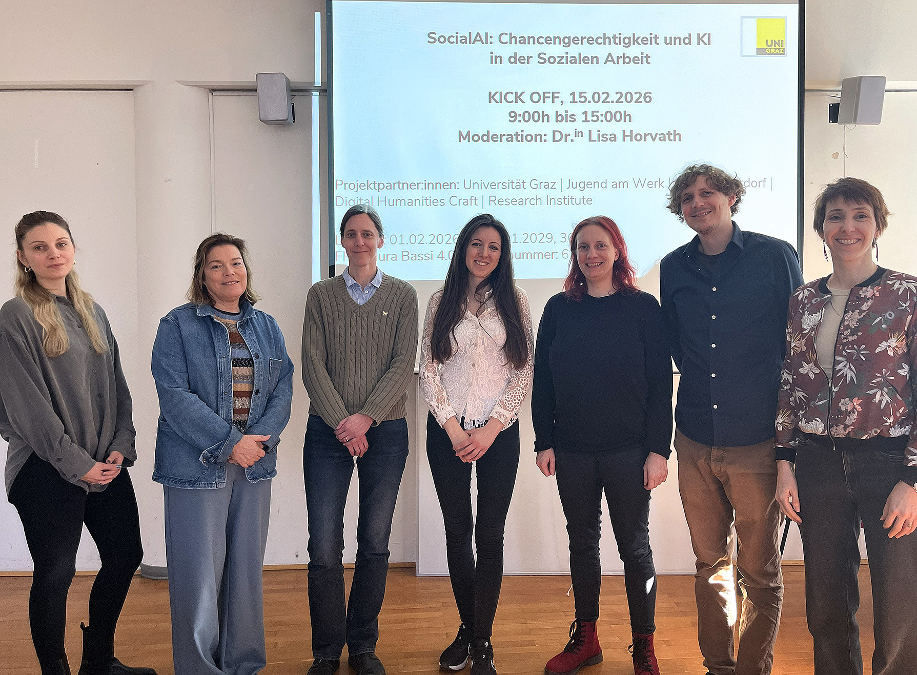 Sechs Frauen und ein Mann stehen in einer Reihe vor einer Leinwand, auf der Infos zum Projekt SocialAI eingeblendet sind 