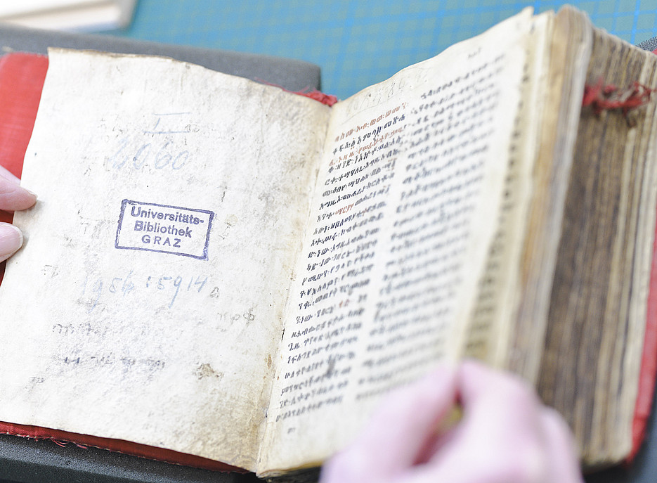 Eine Hand schlägt die Seiten eines Pergament-Manusskripts auf ©Uni Graz/Tzivanopoulos