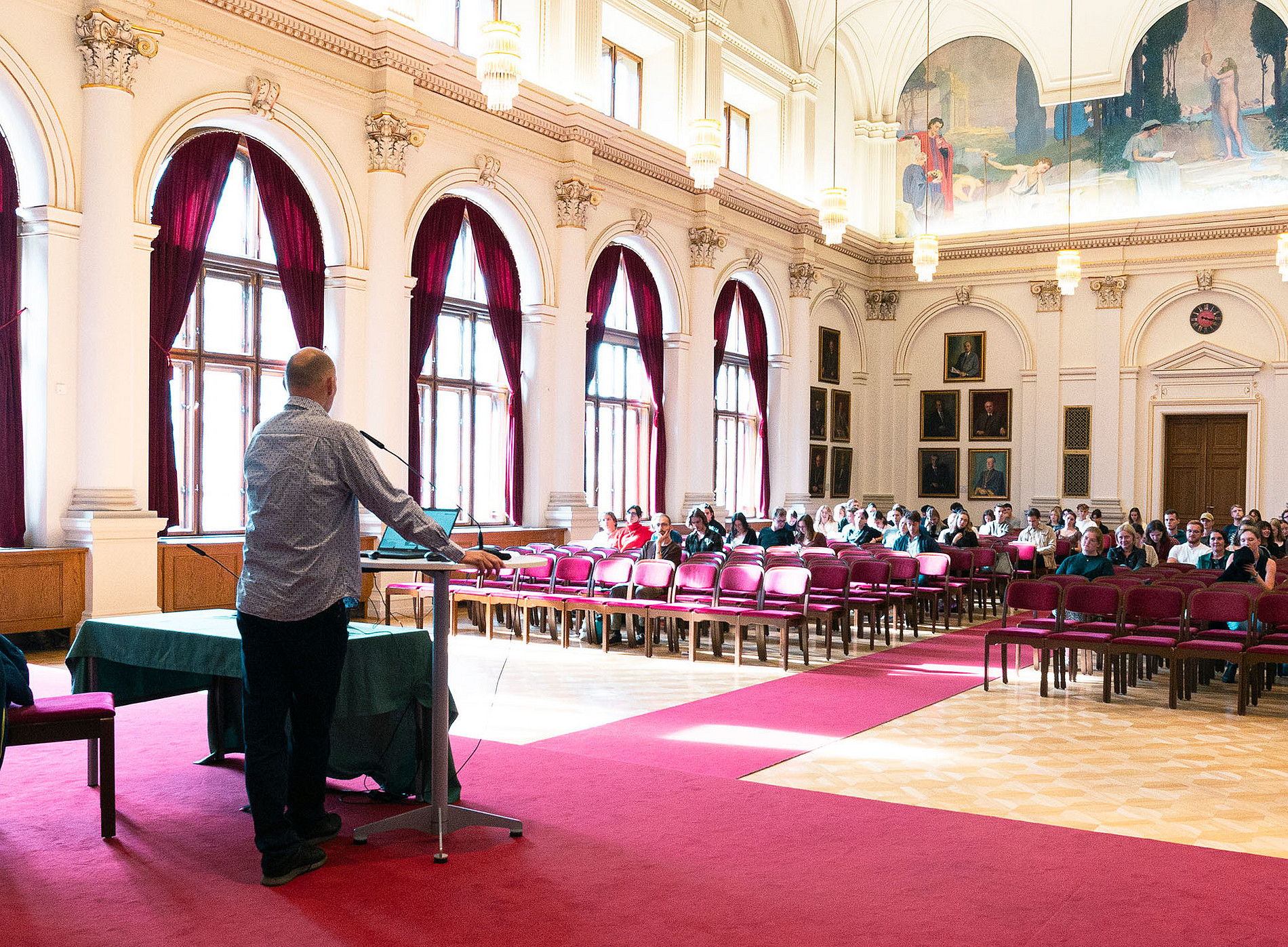 Ein Herr hält einen Vortrag in einem traditionellen Saal mit großen Fenstern. Die Stuhlreihen im Saal sind zur Hälfte mit Personen gefüllt. ©Uni Graz/Angele