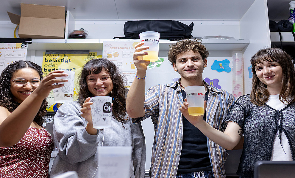 vier junge Personen, die beim Fest Uni vibes ihre Becher in die Höhe heben