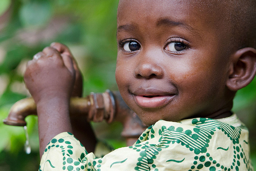 Little African boy clutches a tap