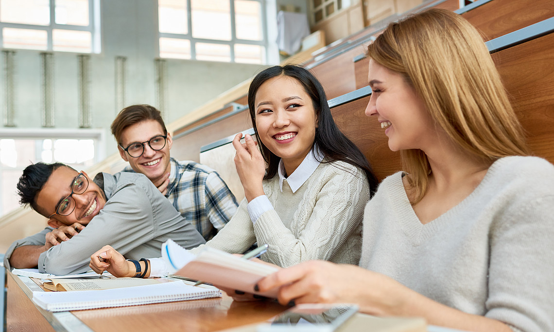 Multi-ethnic group of cheerful students sitting at desks in lecture hall of modern college and laughing