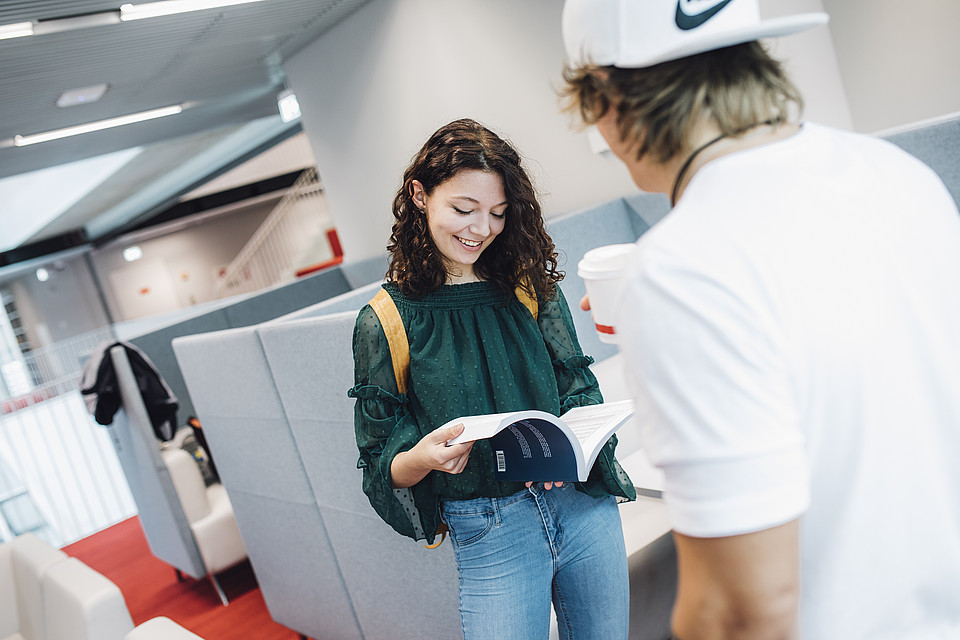 Zwei Studierende unterhalten sich stehen in der Universitätsbibliothek