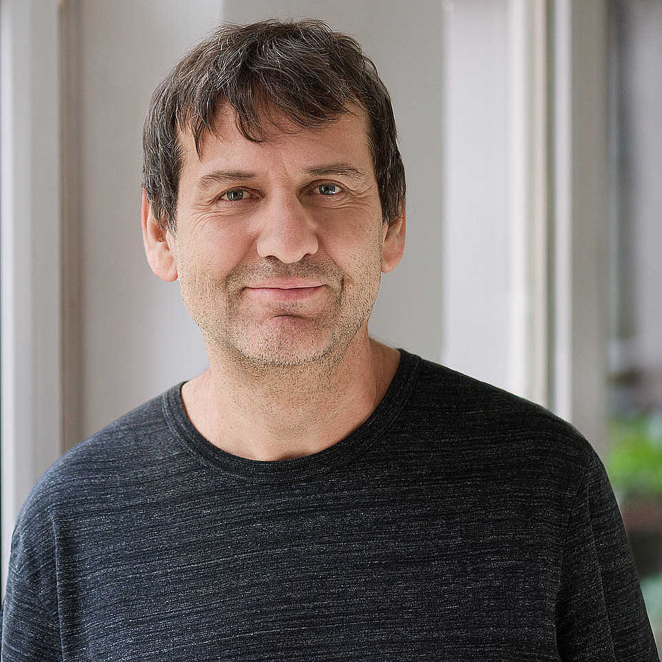 Portraitfoto von einem Mann mit kurzen braunen Haaren in einem schwarzen Pullover