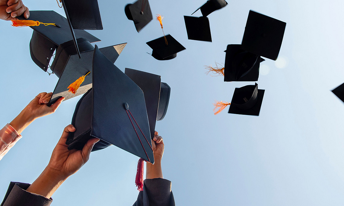 Studierende werfen ihre Abschlusshüte in die Luft.